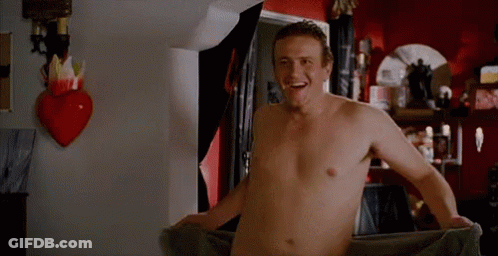 A Shirtless Man Is Wrapped In A Towel In A Room . GIF