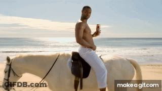 A Shirtless Man Riding A White Horse On A Beach GIF