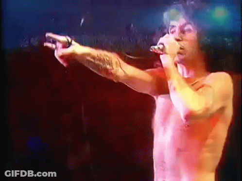 A Shirtless Man Singing Into A Microphone While Pointing GIF