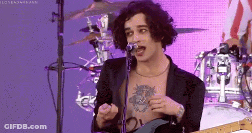A Shirtless Man Singing Into A Microphone With A Tattoo On His Chest GIF