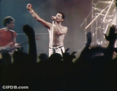 A Shirtless Man Singing Into A Microphone With His Fist In The Air GIF