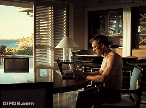 A Shirtless Man Sits At A Table With A Laptop And A Lamp GIF