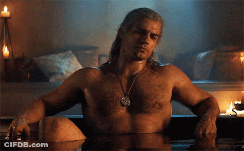 A Shirtless Man Sits In A Bathtub With Candles In The Background GIF