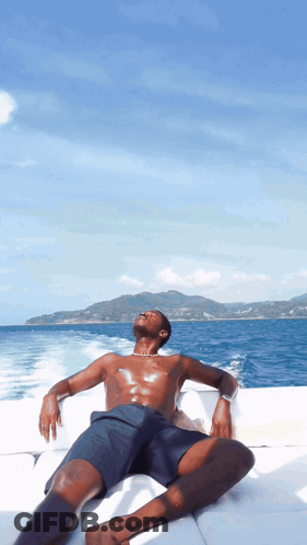 A Shirtless Man Sits On A Boat Looking Up At The Sky GIF