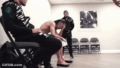 A Shirtless Man Sits On A Chair With His Head Down GIF