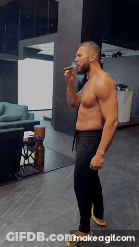 A Shirtless Man Smoking A Cigar In A Living Room With Make A Gif.com On The Bottom GIF