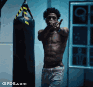 A Shirtless Man Standing Next To A Punching Bag GIF