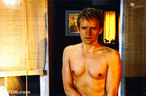 A Shirtless Man Stands In A Bathroom With A Picture On The Wall Behind Him GIF