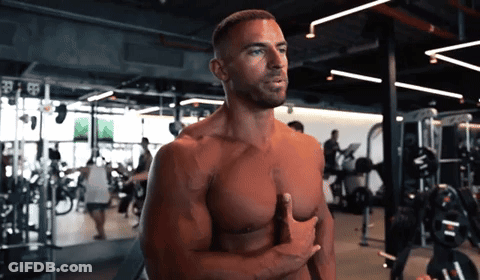 A Shirtless Man Stands In A Gym With His Hands On His Chest GIF