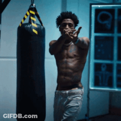 A Shirtless Man Stands In Front Of A Boxing Bag GIF