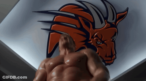 A Shirtless Man Stands In Front Of A Bull Logo On A Wall GIF