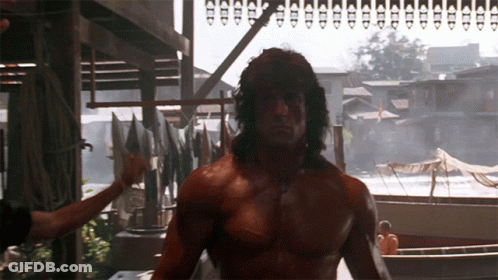 A Shirtless Man Stands In Front Of A Row Of Boats And Buildings GIF