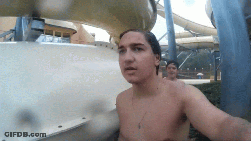 A Shirtless Man Stands In Front Of A Water Slide At A Water Park GIF