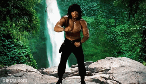 A Shirtless Man Stands In Front Of A Waterfall GIF