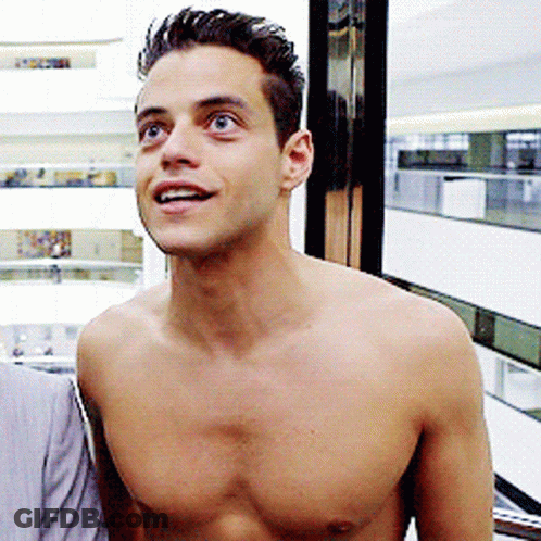 A Shirtless Man Stands In Front Of A Window And Smiles GIF
