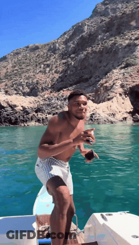 A Shirtless Man Stands On A Boat In The Ocean GIF