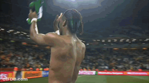 A Shirtless Man Stands On A Soccer Field In Front Of A Donald 'S Sign GIF