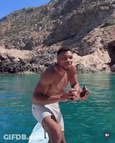 A Shirtless Man Stands On A Surfboard In The Water With The Date 18/18 In The Corner GIF