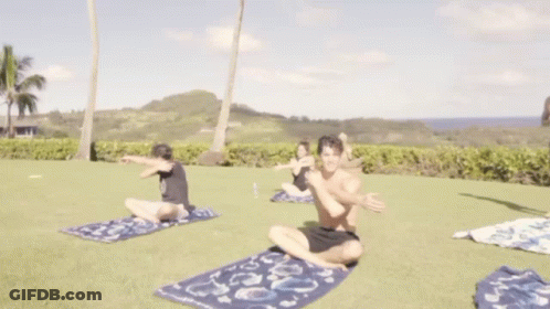 A Shirtless Man Stretches His Arms While A Woman Sits On The Grass GIF