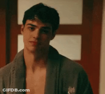A Shirtless Man Wearing A Bathrobe Is Standing In Front Of A Door . GIF