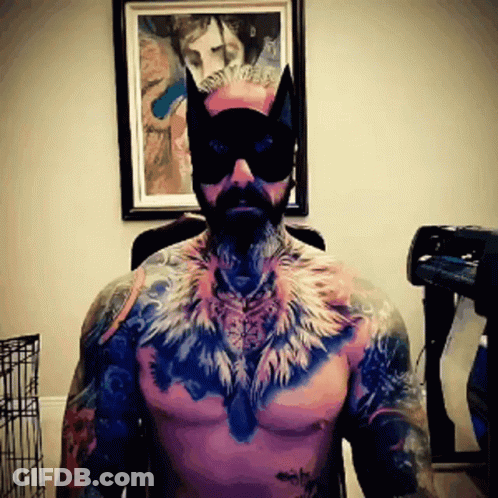 A Shirtless Man Wearing A Cat Mask And Feathers On His Chest GIF