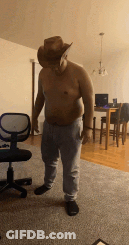 A Shirtless Man Wearing A Cowboy Hat And Sweatpants Stands In A Living Room GIF