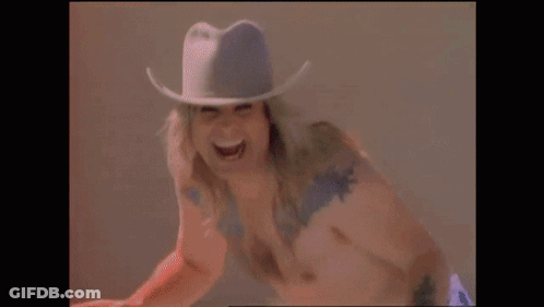 A Shirtless Man Wearing A Cowboy Hat Is Laughing . GIF