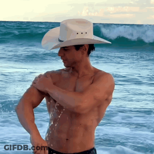 A Shirtless Man Wearing A Cowboy Hat Is Standing In The Ocean GIF