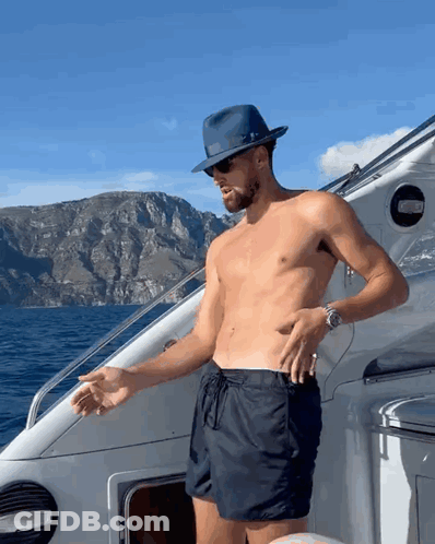 A Shirtless Man Wearing A Hat And Sunglasses Stands On A Boat GIF