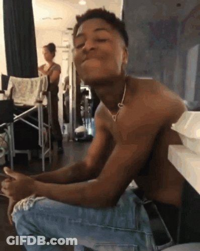 A Shirtless Man Wearing A Heart Shaped Necklace Is Sitting On The Floor GIF
