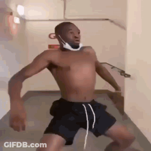 A Shirtless Man Wearing A Mask And Shorts Is Standing In A Hallway . GIF