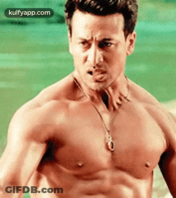 A Shirtless Man Wearing A Necklace And A Pendant On His Chest . GIF