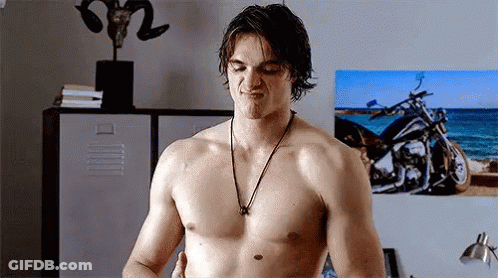 A Shirtless Man Wearing A Necklace Is Standing In Front Of A Picture Of A Motorcycle . GIF