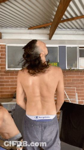 A Shirtless Man Wearing A Pair Of Champion Shorts Stands In Front Of A Brick Wall GIF