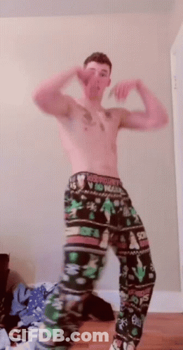 A Shirtless Man Wearing A Pair Of Christmas Pajamas GIF