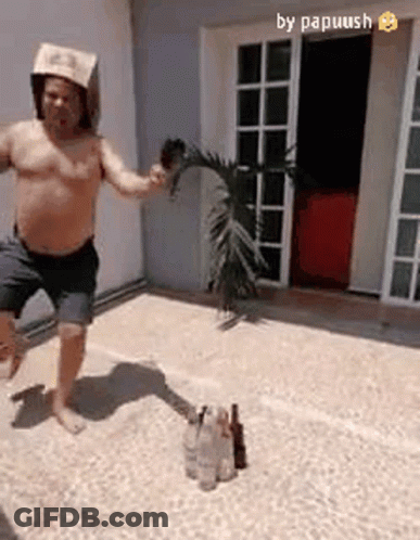 A Shirtless Man Wearing A Paper Hat Is Jumping In The Air While Holding A Palm Tree Branch . GIF