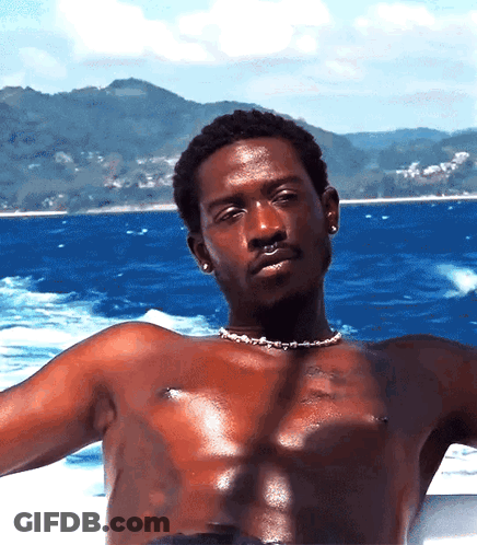 A Shirtless Man Wearing A Pearl Necklace Is Sitting On A Boat In The Ocean GIF