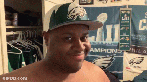 A Shirtless Man Wearing A Philadelphia Eagles Hat Looks At The Camera GIF
