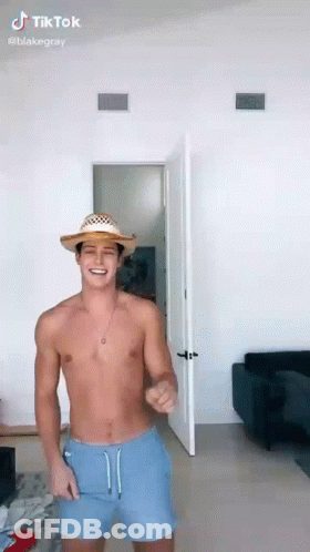 A Shirtless Man Wearing A Straw Hat And Blue Shorts Is Dancing In A Room . GIF