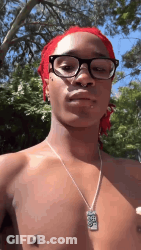 A Shirtless Man Wearing Glasses And A Necklace Is Standing In Front Of Trees . GIF