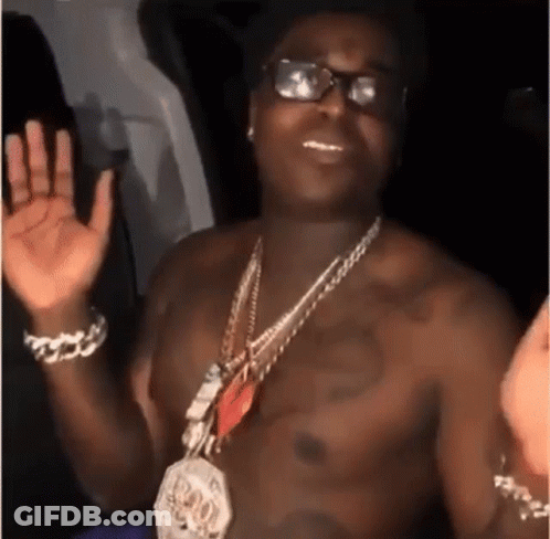 A Shirtless Man Wearing Glasses And A Necklace Is Waving His Hands . GIF
