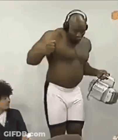 A Shirtless Man Wearing Headphones And Shorts Is Standing In Front Of A Camera . GIF