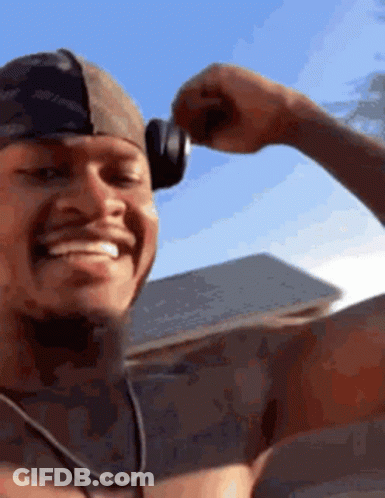 A Shirtless Man Wearing Headphones Is Smiling And Flexing His Arm . GIF
