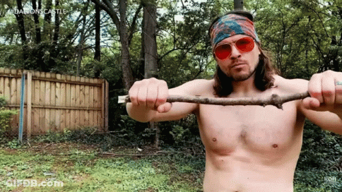 A Shirtless Man Wearing Sunglasses And A Bandana Is Holding A Stick In His Hands GIF