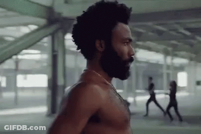 A Shirtless Man With A Beard And Afro Is Standing In A Building . GIF