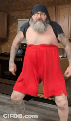 A Shirtless Man With A Beard And Red Shorts Is Dancing GIF
