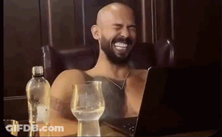 A Shirtless Man With A Beard Is Laughing While Sitting In Front Of A Laptop . GIF
