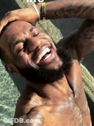 A Shirtless Man With A Beard Is Laughing With His Eyes Closed And His Hand On His Head . GIF