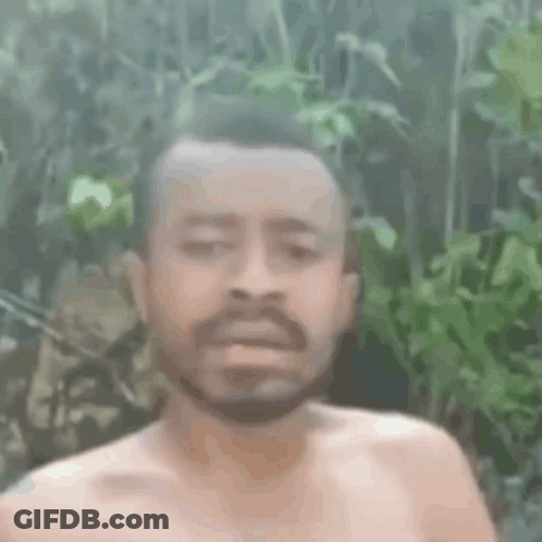 A Shirtless Man With A Beard Is Making A Funny Face In Front Of Trees . GIF