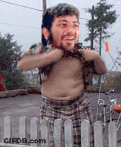 A Shirtless Man With A Beard Is Standing Behind A Fence GIF